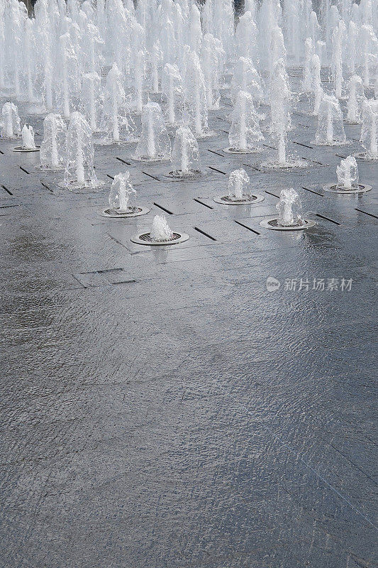 公园花园铺路板上的路面喷水池/湿砖铺路水景，喷水池的水溅在铺路石上，让孩子们在夏天玩耍和淋湿，多个喷水池和水滴倾泻而下